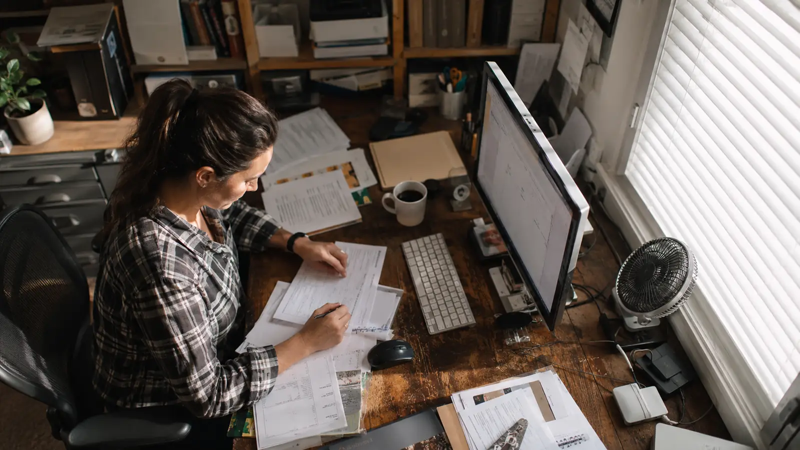 USB desk fan rotated to blow across a cluttered desk covered in papers and cables