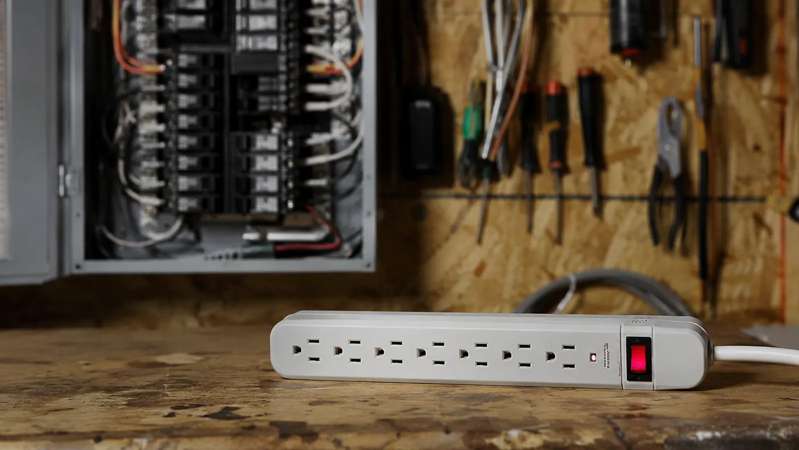 A cluttered breaker panel and a power strip side by side on a workbench, representing the electrician's view of home power problems