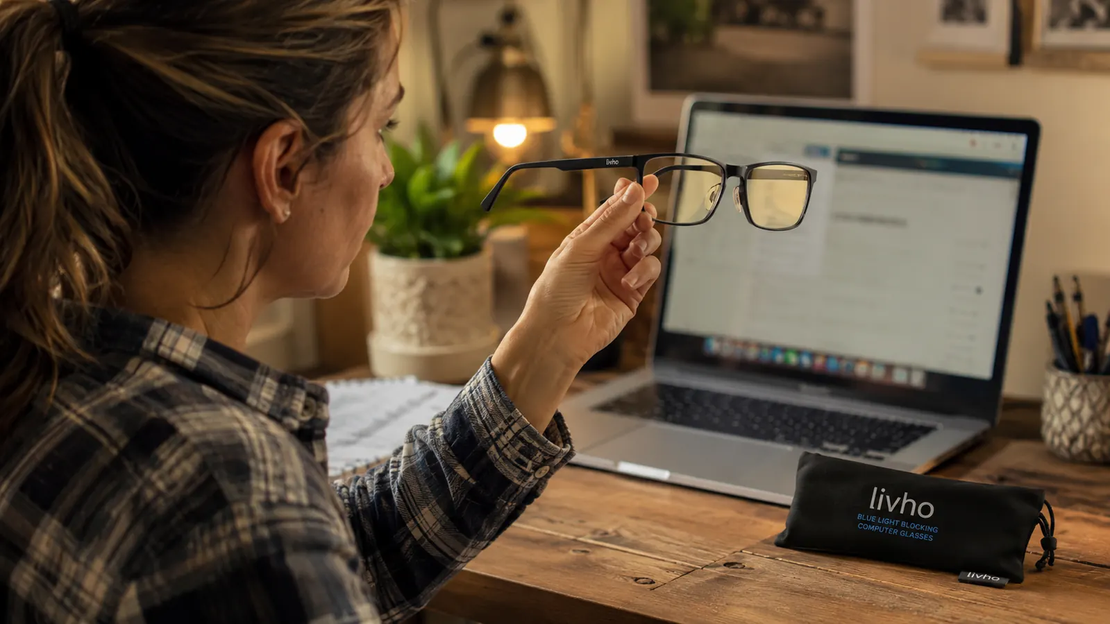 Close up of a hand holding a pair of livho blue light blocking glasses over a laptop keyboard
